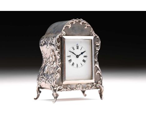 An Edwardian boudoir clock; white enamel rectangular dial with Roman numerals; set within an arched silver case, the sides de