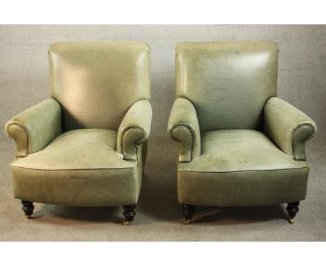 A pair of contemporary light green leather club armchairs, with scrolling arms, on turned legs terminating in brass castors. 