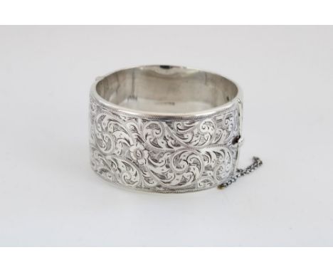 C20th hallmarked hinged silver bangle with safety chain, front with chased scroll and flower decoration, internal W6cm, gross