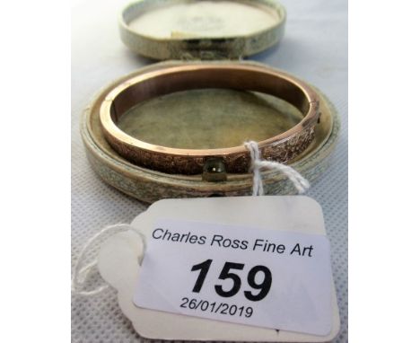 A 9ct rose gold hinged bangle, one half having engraved scroll decoration.