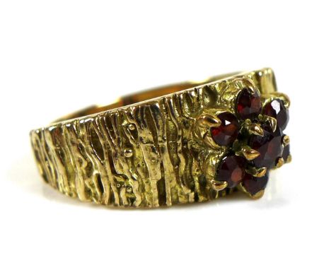 A 9ct gold and garnet ring, bark effect to band with garnets set in a flowerhead, circa 1970's, size O/P, marked 9ct, 6.8g. 