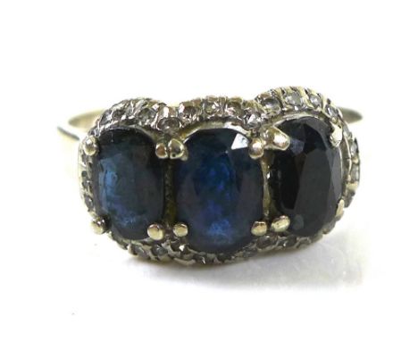 A 14ct white gold dress ring, set with three dark blue sapphires, each 5.7 by 4.6mm, with diamond brilliants surrounding, siz