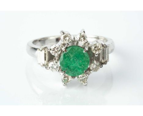 An emerald and diamond cluster ring, the circular mixed-cut emerald claw set within a border of round brilliant-cut diamonds,