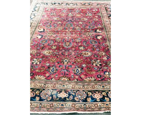 An Oriental burgundy-ground hand-woven multi-coloured wool drawing room rug with floral decoration, double borders and short 