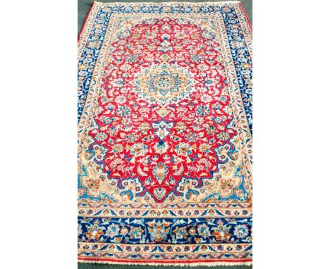 An Oriental scarlet-ground hand-woven multi-coloured wool drawing room rug with floral decoration, double borders and short f
