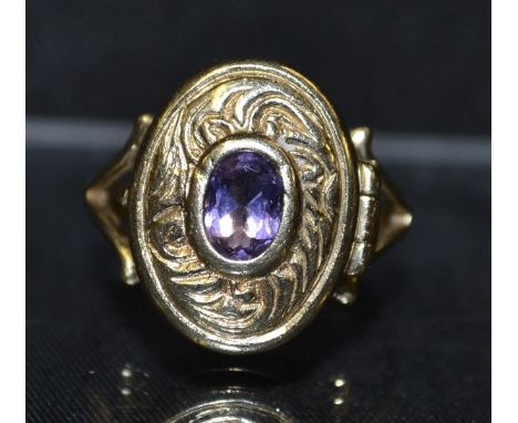 A contemporary poison ring, oval hinged top inset with a single amethyst within floral scrolling surround, open shoulders, 9c