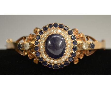 A diamond & sapphire hinge bangle, central oval blue cabochon sapphire approx 8.2ct, surround by two stepped bands of twenty 