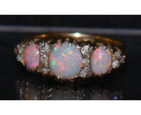 An Edwardian opal and diamond ring, central oval opal doublet, flanked by a smaller conforming opal to each side, all flashin