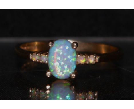 An opal ring, central oval opal, flashing blue and green colour play, flanked to each side by pairs of conforming opal accent