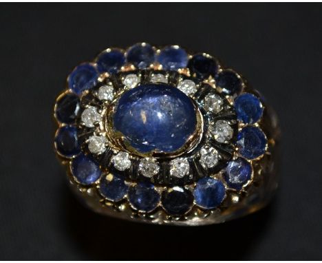 A diamond & sapphire cluster ring , central oval blue cabochon sapphire, approx 1ct, surround by two stepped bands of twelve 
