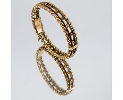 A gold hinged bangle, unmarked, the barley twist borders enclosing the bead centre, internal diameter 5.9cm, 22g gross, tests
