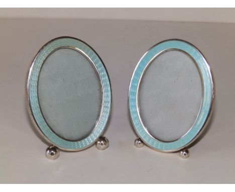 A small pair of enamelled oval Sterling silver photo frames, having pale turquoise guilloche enamel borders, on ball feet - '