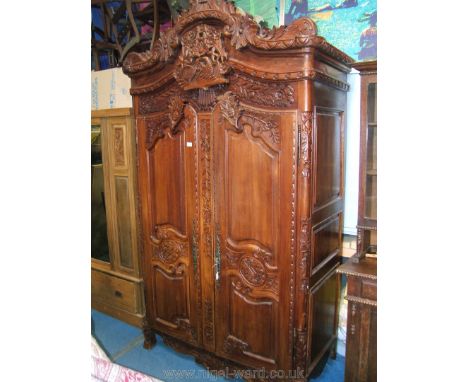 An ornate French Cherrywood Armoire, having arch top, highly carved pediment top with central carved panel with flowers and b
