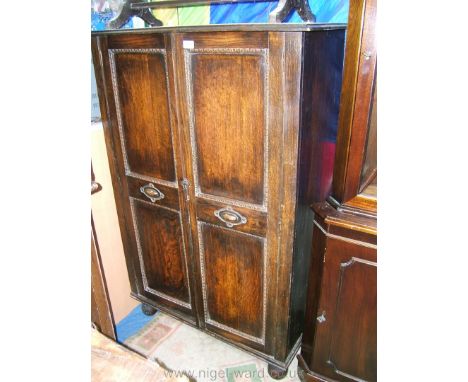 A 1920's Oak Hall Cupboard having opposing pair of two panel doors with applied, carved mouldings and carved central motifs, 