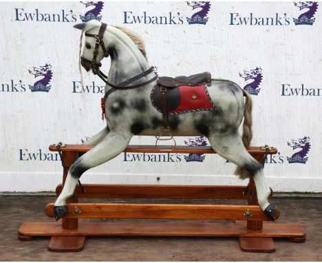 A modern wooden rocking horse. Dapple grey colour with leather saddle and bridal wear on a wooden swing frame base.  110cm hi