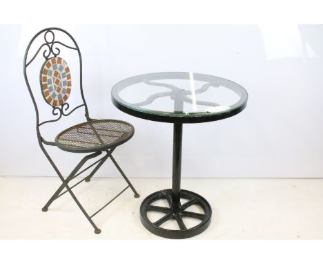 A rustic wrought iron garden chair with mesh seat together with a glass topped table. 