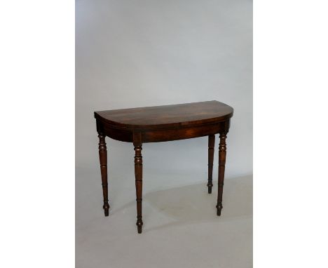 A George IV rosewood veneered card table of D-shape with yew veneered border, the frieze with strung frame on turned tapered 
