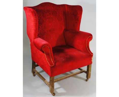 A George III style mahogany wingback armchair of conventional design on square legs joined by an H-stretcher, ceramic castors