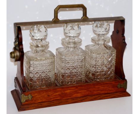 An oak three bottle tantalus with silver plated mounts, each decanter hobnail cut, 34cm wide, 29cm high, early 20th Century (