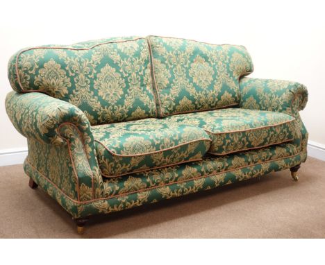 Traditional two seat sofa, scrolled arms, turned supports on brass castors, upholstered  in green and gold fabric with a flor