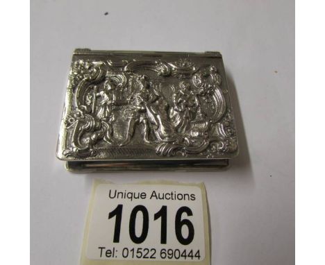 A snuff box in white metal with embossed figures to front.