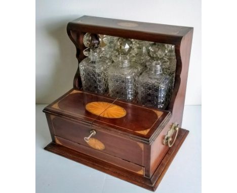 An Edwardian Sheraton revival Tantalus/games box, with three cut-glass bottles concealed by mirrored fan-inlaid hood behind a