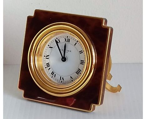 A CARTIER travel or alarm clock, the white enamel dial with black Roman numerals within a reeded bezel on a tortoiseshell-eff