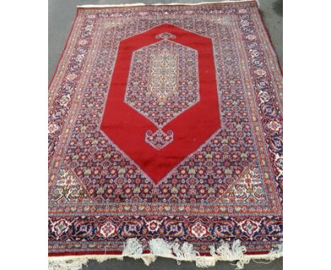 An Oriental hand-knotted multi coloured burgundy-ground wool rug with double border and long fringe, in good condition, light