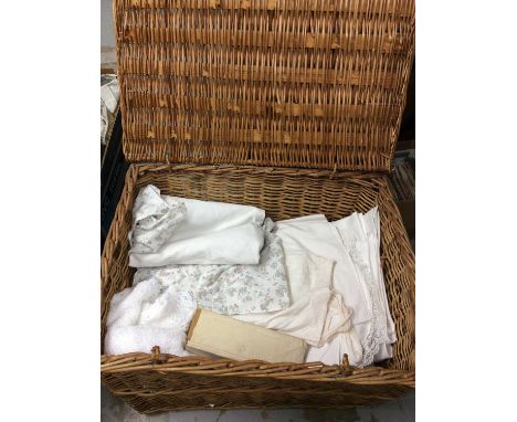 Wicker hamper containing various textiles, table linens, blankets and vintage suitcase 