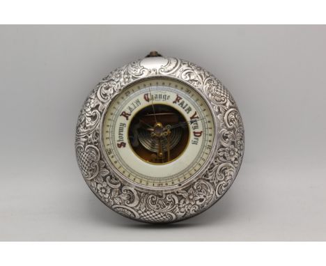 An early 20th century silver covered wooden cased aneroid barometer, marks rubbed, with floral leaf and scroll embossed ornam