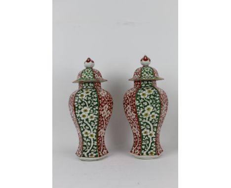A pair of Chinese, early 20th century hexagonal vases and covers, each decorated with panels of blossoming trees on an altern