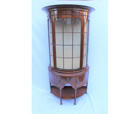 An early 20th century mahogany bow fronted display cabinet, with inlaid ornament, a glazed panel door and sides, over a drawe