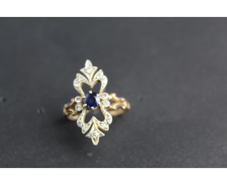 A diamond and sapphire ring set with a central blue sapphire, 4.6mm and fourteen diamonds on a shaped frame and scrolled shou