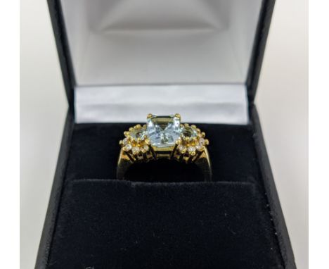 AN 18CT GOLD AQUAMARINE AND DIAMOND SET DRESS RING, set with one large aquamarine and two smaller stones, with diamond surrou