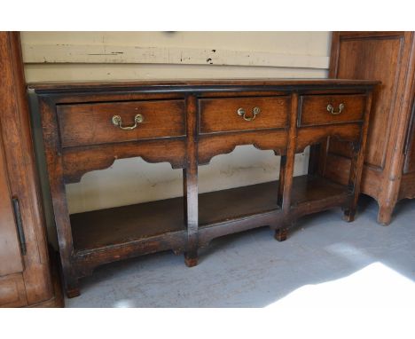 Small George III oak dresser base, the moulded top above three drawers with brass swan neck handles, shaped frieze, square cu