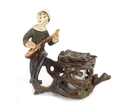 An early 20th cold painted lead inkwell, modelled as an elfin figure playing a banjo, aside a branch entwined ceramic well, 7