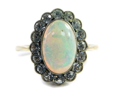 A 9ct gold opal dress ring, the central oval opal in platinum rub over setting, surrounded by tiny white stones, on a raised 