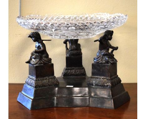 Large bronze table centre having an engraved and cut glass dish supported by three cherubs and standing on a triform base   C
