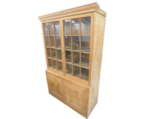 A stripped pine bookcase, the top with a moulded cornice above two astragal glaze doors, enclosing various compartments, the 