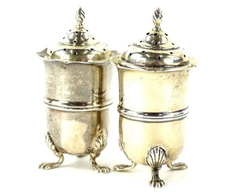A pair of Edwardian silver pepper pots, each with a flame finial a cylindrical body with central moulded band on three shell 