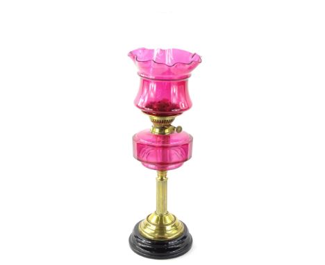 A Victorian brass oil lamp, with cranberry tinted shade and reservoir on reeded column with ceramic base (reservoir AF), 65cm