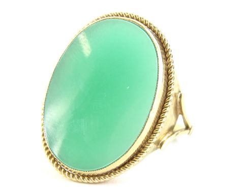 A 9ct gold and jade dress ring, the oval jade in rub over setting, 1.8cm x 2.5cm, with a reeded design border, with V split s