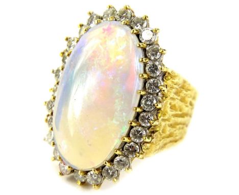 An opal and diamond dress ring, set with central elongated oval imitation opal 2cm x 1.5cm, surrounded by twenty six diamonds