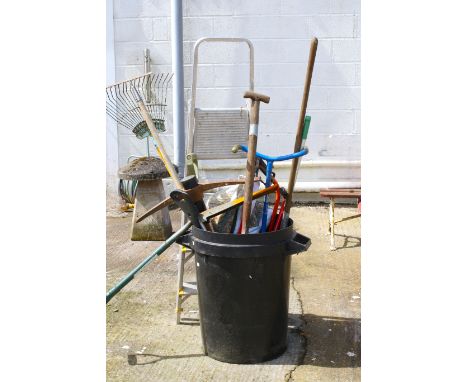 An assortment of garden tools. Including a saw, rake, spade, pickaxe, foldable ladder, etc.