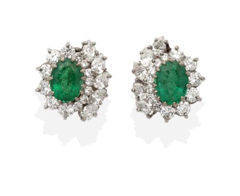 A Pair of 18 Carat White Gold Emerald and Diamond Cluster Clip Earrings, an oval cut emerald in a claw setting, within a bord