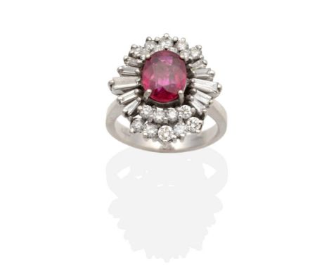 A Ruby and Diamond Cluster Ring, an oval cut ruby in a claw setting, within a two tier border of round brilliant cut and tape