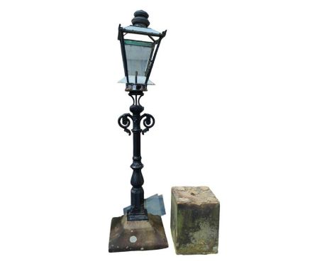 A black painted metal electric garden light in the form of a Victorian gas lamp on concrete base