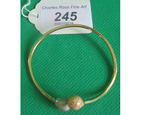A two coloured gold bangle with textured ball terminals marked 750.