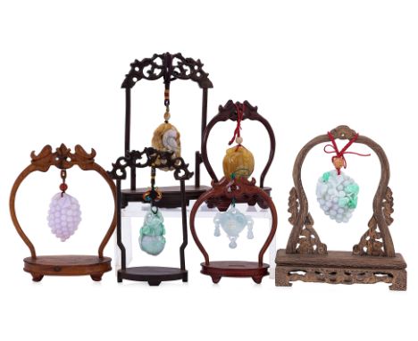 A GROUP OF SIX CARVED JADE PENDANTS ON STANDS
To include two modelled as a bunch of grapes; one carved with a phoenix; a doub