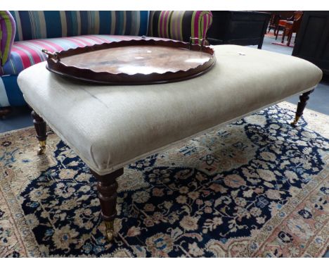 A LARGE REGENCY STYLE BANQUETTE STOOL WITH RING TURNED TAPERED LEGS ENDING IN BRASS CASTORS. W.146cms.
